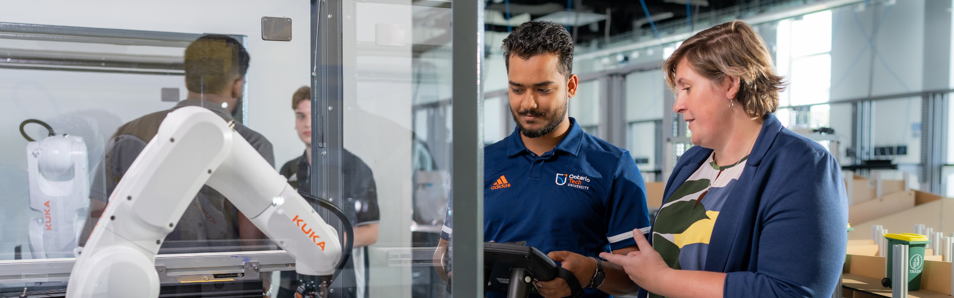 Female professor assisting male student on robotic arm 